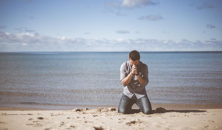 homem ajoelhado e rezando na beira da praia
