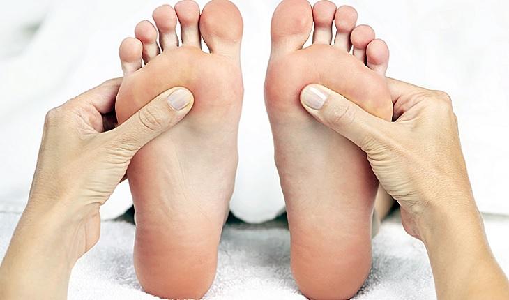 A foto mostra uma mulher recebendo massagem nos pés