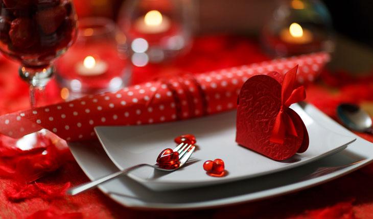 mesa decorada na cor vermelha, com guardanapo, mini corações de plástico, velas, e caixinha de presente em forma de coração