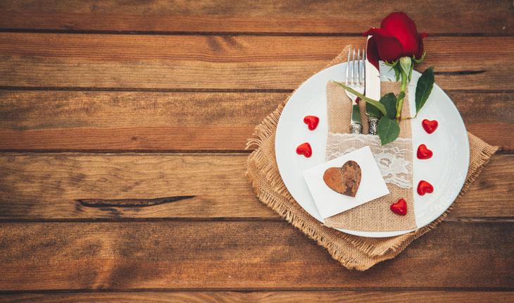 mesa com prato branco decorado com uma rosa e corações vermelhos de papel