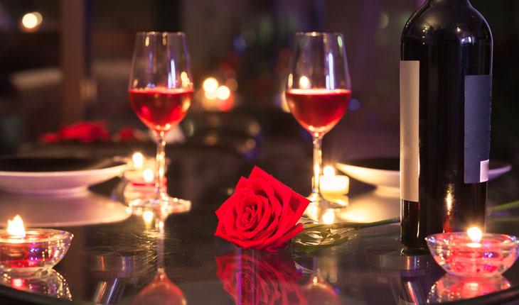 mesa de dia dos namorados com duas taças de vinho, uma rosa vermelha, pratos brancos