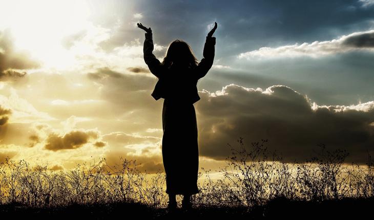 silhueta de uma mulher com os braço erguidos par ao céu durante o pôr do sol