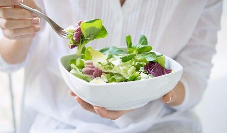 Na foto há uma mulher comendo salada em um pote branco