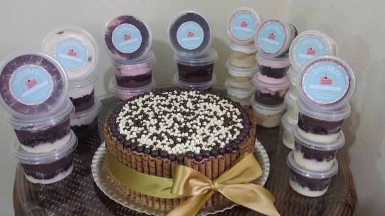 Produtos da confeitaria Doceres, da proprietária Aylla, com um bolo ao centro, acompanhado de bolos no pote em diversos sabores