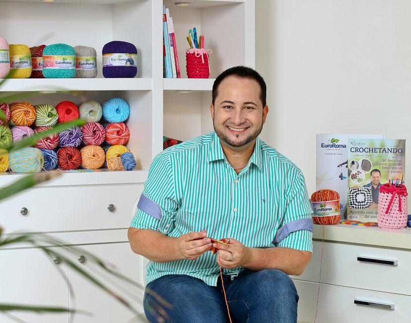 Marcelo Nunes está sorrindo enquanto segura fios de crochê em sua mão