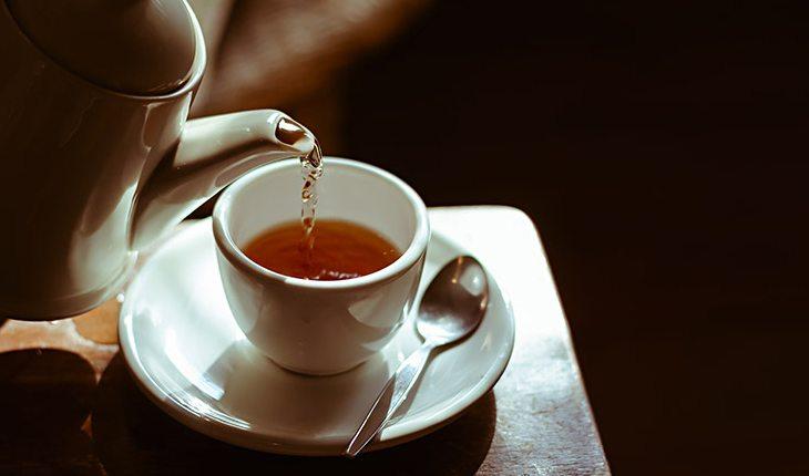 Na foto há uma pessoa despejando chá de um bule em uma xícara
