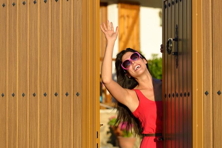 Happy woman opening her country house door to welcome guests visitors. Charming caucasian brunette girl good bye standing in home entrance.