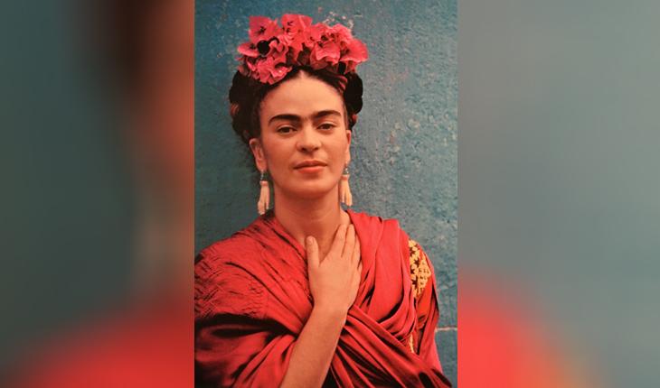 Frida com vestimentas e adereços vermelhos, com a mão no pescoço, posa para foto