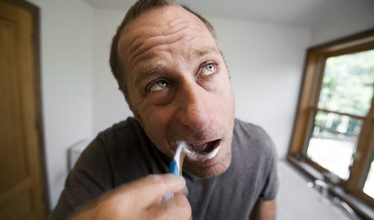 A foto mostra um homem escovando os dentes