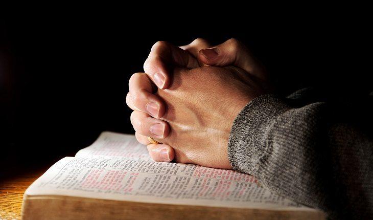 Mãos em prece sobre a bíblia pedindo auxílio pelo poder da fé