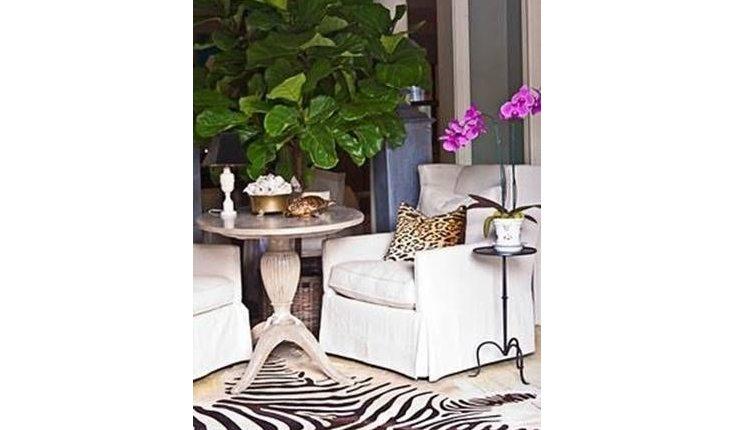 Sala com um tapete de zebra e uma poltrona branca com uma almofada de animal print de onça em cima.
