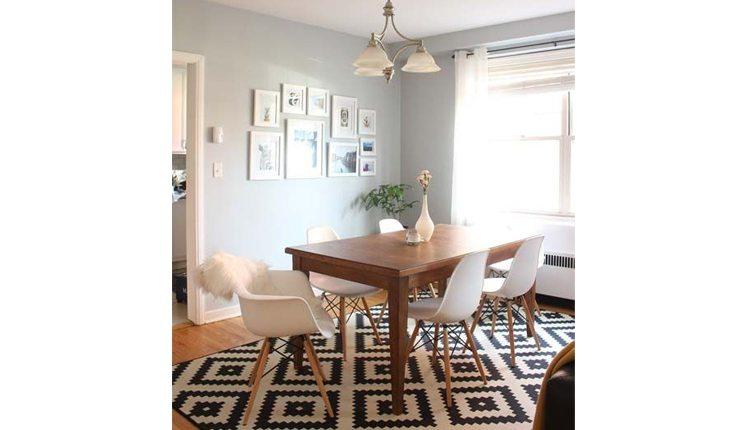 Sala de jantar com a mesa de madeira e cadeiras brancas e com um tapete branco e peto com desenhos geométricos