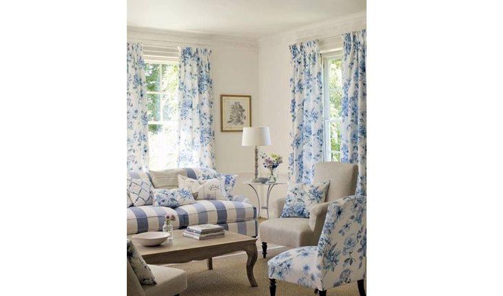 Sala com sofá estampado em branco e azul bebê e com almofadas florais também em azul bebê. As cortinas e uma poltrona têm a mesma estampa.