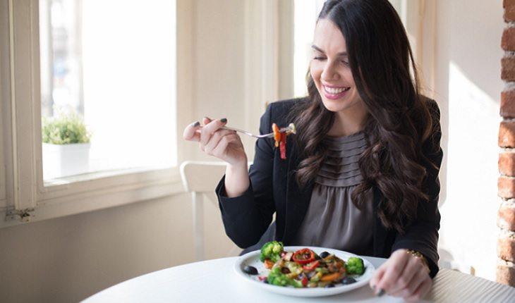 A foto mostra uma mulher comendo salada sorrindo