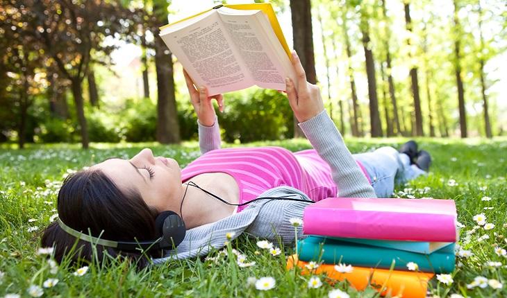 A foto mostra uma mulher deitada em um gramado lendo. Ler livros com línguas que não está acostumada é um bom exercício para o cérebro