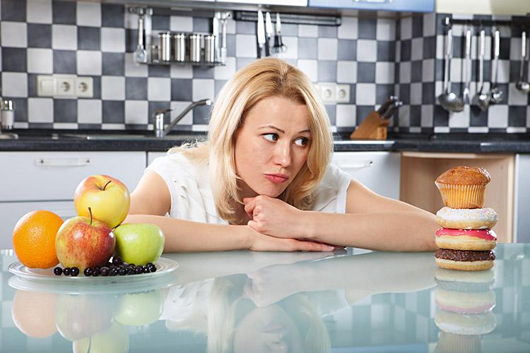 Mulher dividida entre comer doces ou frutas