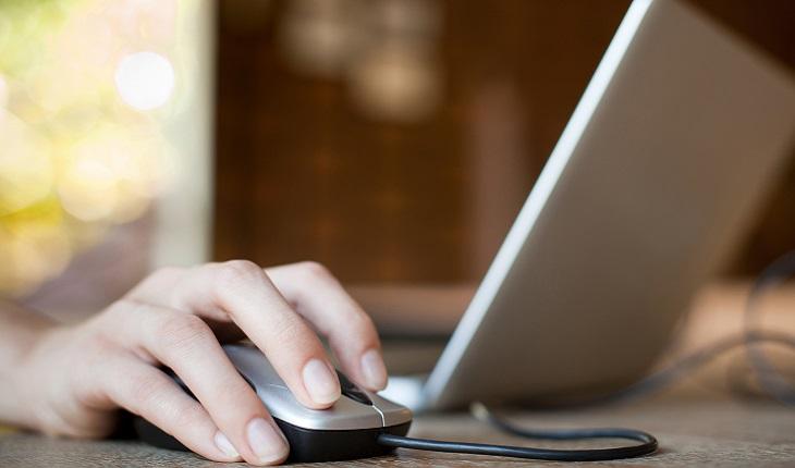 A foto mostra uma mulher mexendo no computador com mouse. Utilizar a mão que não está acostumada para isso ajuda a exercitar o cérebro