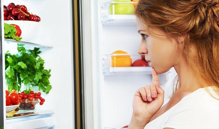 mulher olhando dentro da geladeira enquanto pensa no que vai comer