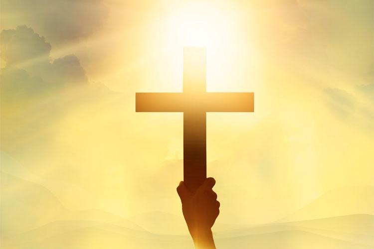 Imagem de uma mão segurando uma cruz com o sol ao fundo