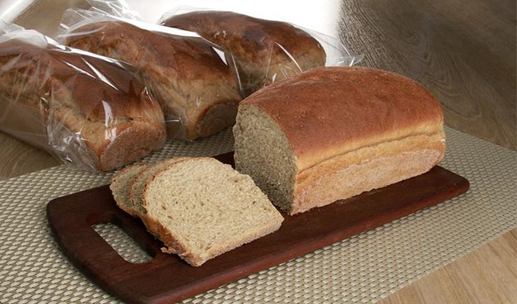 pão integral cortado em uma tábua e três peças ainda embaladas em saquinhos transparentes