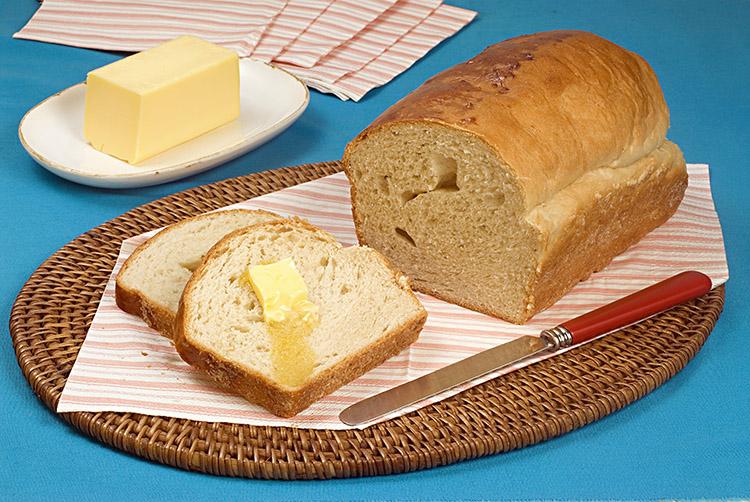 Pão saboroso caseiro, toalha de mesa azul, faca, manteiga ao lado.