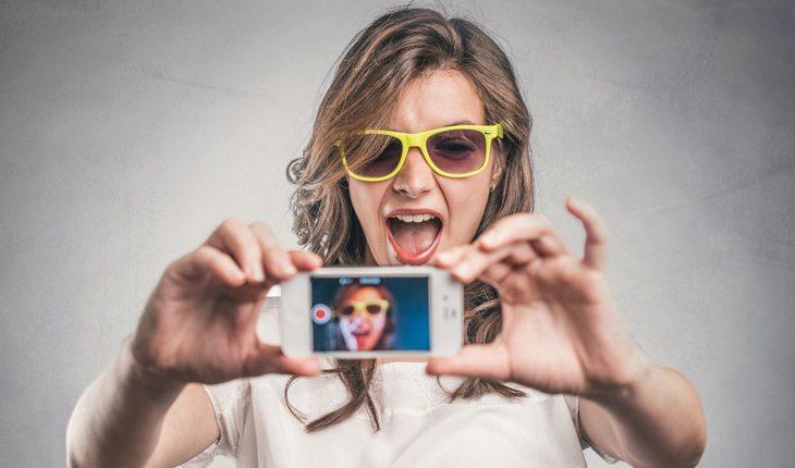 mulher tirando uma selfie sorrindo e com óculos colorido