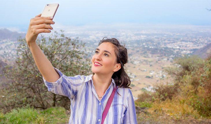 mulher tirando selfie com uma paisagem ao fundo