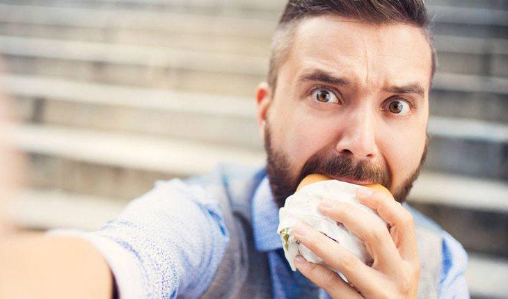 homem tirando selfie enquanto come um hamburguer