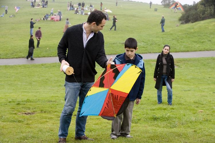 um homem de casaco preto e uma criança segurando uma pipa vermelha, amarela e azul