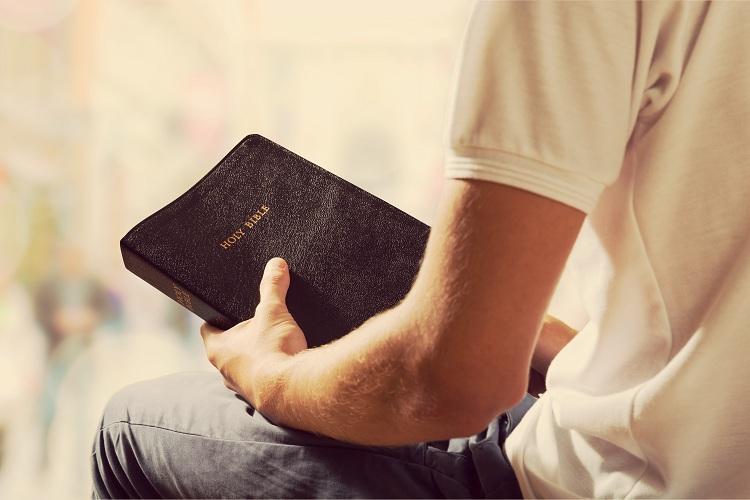 Homem de camiseta branca segurando uma bíblia marrom código