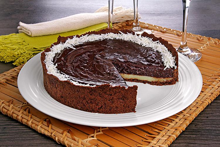 Torta de chocolate com coco em um prato de servir branco com um pedaço já retirado.