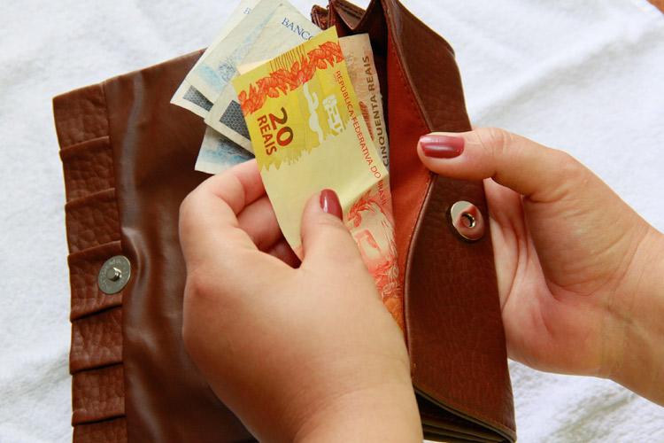 Mão feminina colocando dinheiro dentro da carteira