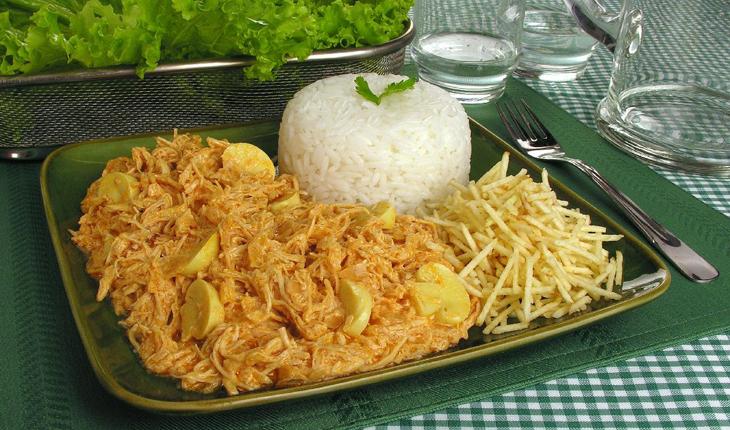 estrogonofe com frango desfiado servido com bata palha e arroz em um prato preto