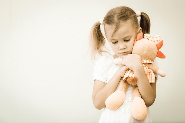 criança triste abraçada com boneca