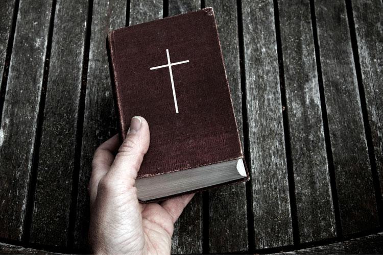 Mão segurando uma Bíblia sobre uma mesa