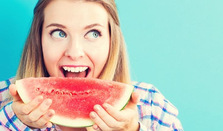 A foto mostra uma mulher comendo um pedaço de melancia para manter uma alimentação saudável e seu cérebro jovem