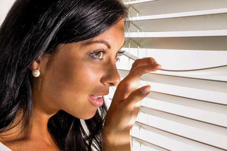 mulher espiando pela janela dentro da sua casa