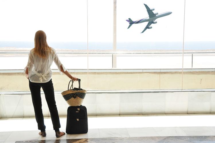 Mulher segurando mala vendo avião decolar em aeroporto