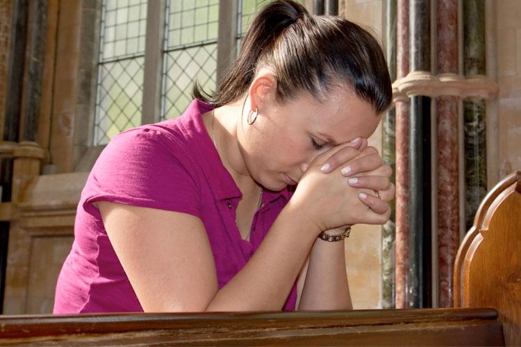 Mulher rezando ajoelhada na igreja