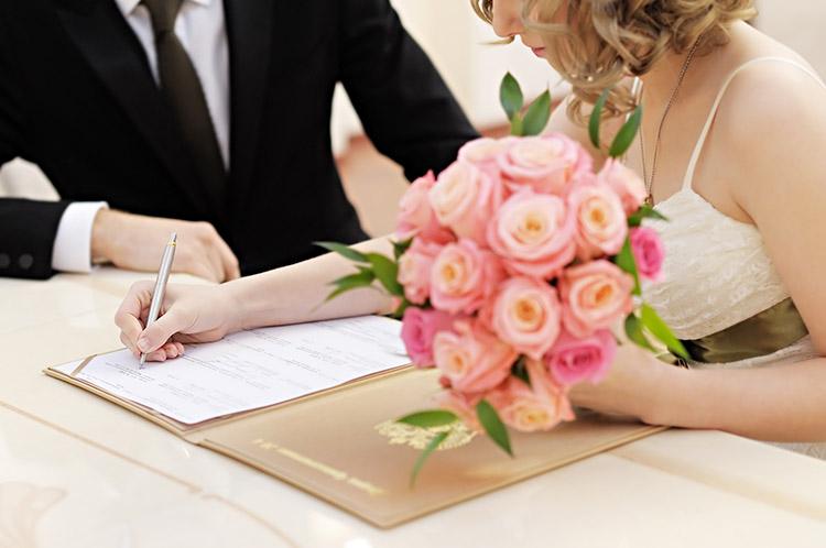 casal assinando contrato de casamento com buquê rosa em evidência