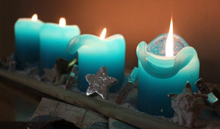 quatro velas azuis grossas e pequenas acesas em um suporte com pequenos anjos de porcelana