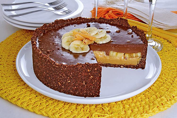 Torta de banana com doce de leite e chocolate em um prato branco com um pedaço faltando.