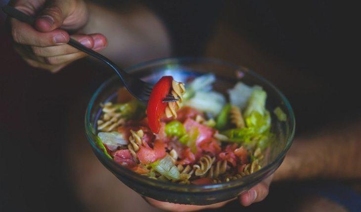 pessoa comendo salada com macarrão e legumes em um bowl de vidro