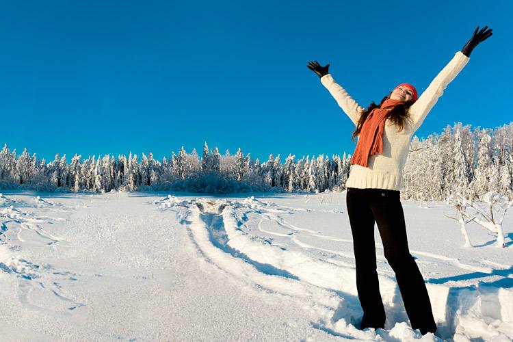 mulher com roupa de frio e braços abertos na neve e com árvores cobertas de neve ao fundo