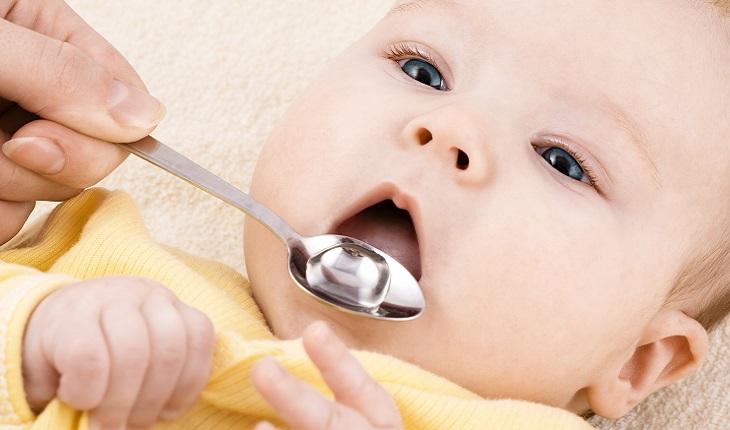 A foto mostra um bebê tomando remédio de homeopatia em uma colher