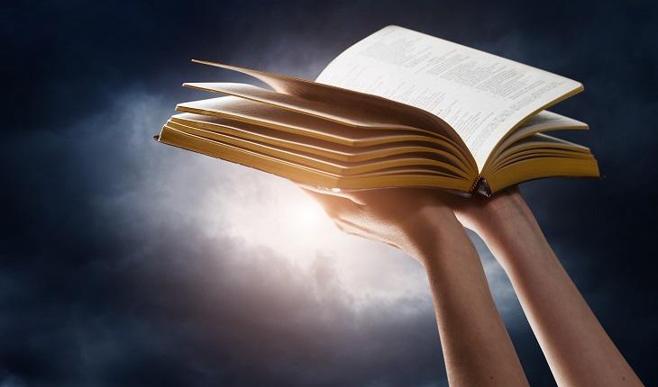 A foto mostra uma mulher levantando uma Bíblia aberta em direção ao céu, como se tivesse pedindo a ajuda de Deus, anjos e santos para o exorcismo