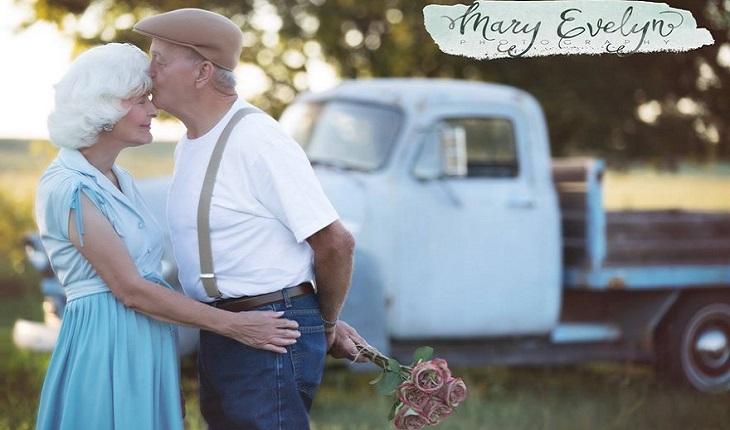 A foto mostra um casal de idosos em frente a um caminhão se beijando