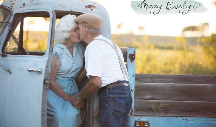 A foto mostra um casal de idosos se beijando de forma romântica encostados em uma camionete azul clara