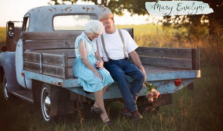 A foto mostra um casal de idosos sentados na traseira de uma camionete azul