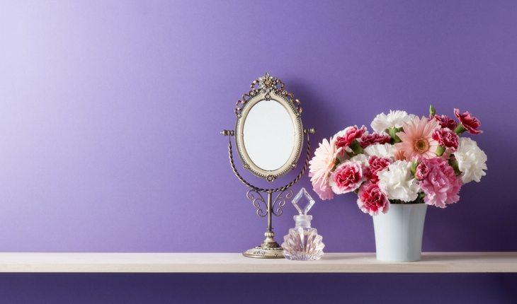 Quarto com parede roxa e cômoda com espelho, perfume e vaso de flores